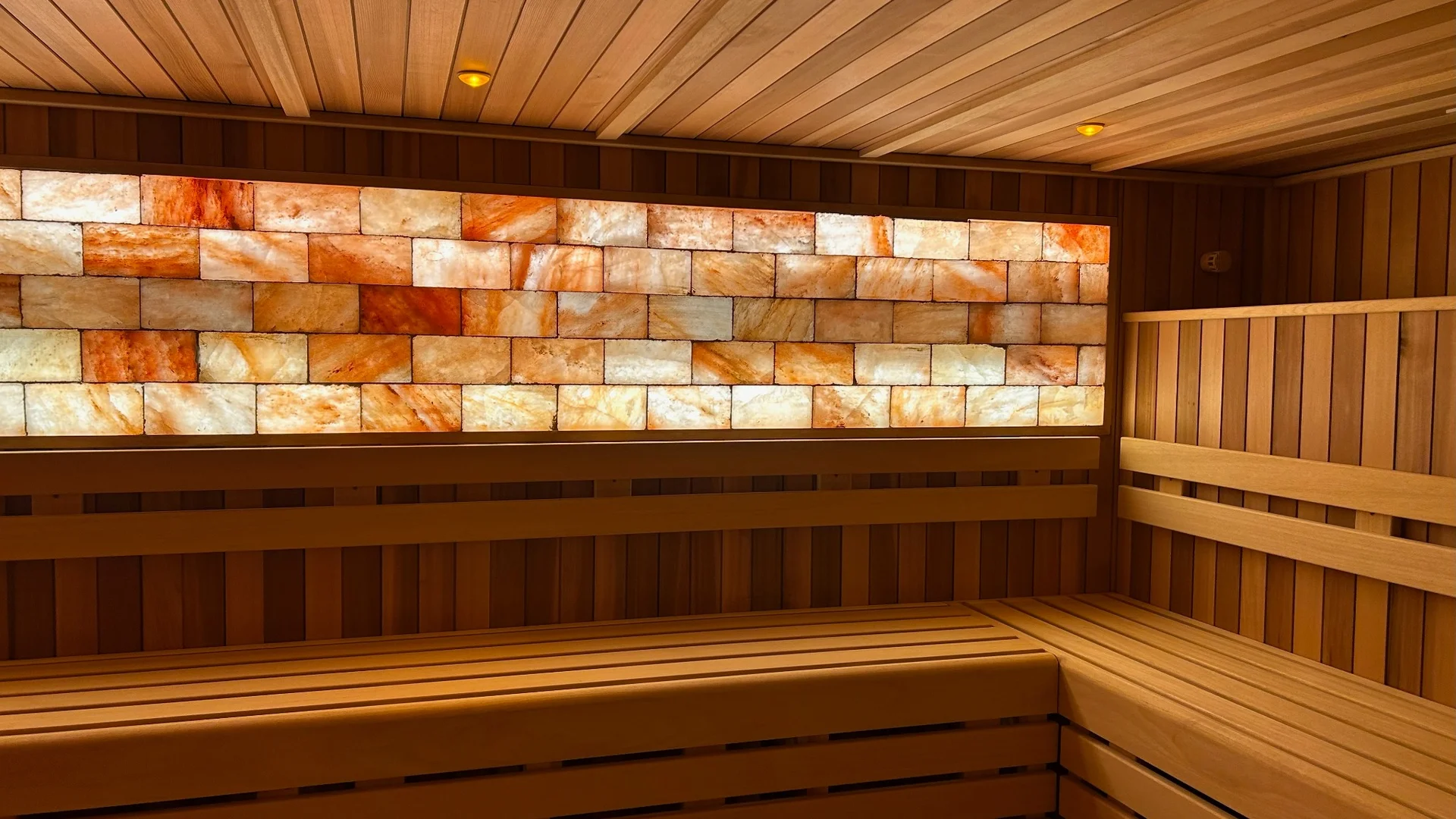 Premium sauna interior featuring an illuminated Himalayan salt wall, timber benches and warm ambient lighting.