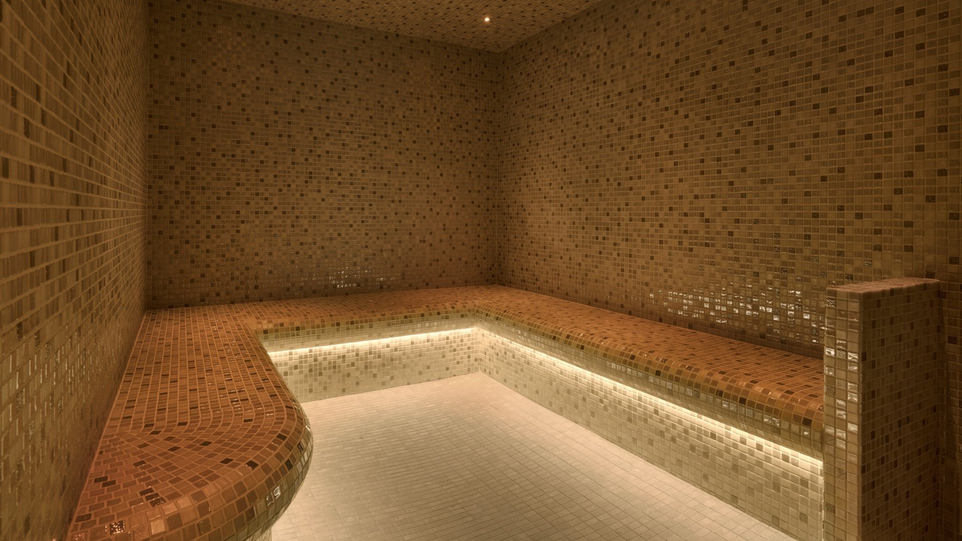 Luxury steam room at The Grand Brighton featuring mosaic finishes, heated bench seating and integrated ambient lighting.